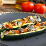 Två halvor av fylld zucchini med fisk och grönsaker på en mörk tallrik.
