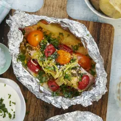 En saftig laxsida i foliepaket med tomater och örter, redo att grilla. Serveras med potatis och en krämig sås.