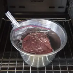 Rostbiff sous vide i en skål med vatten, klämd med en klädnypa, placerad på en ugnsgaller.