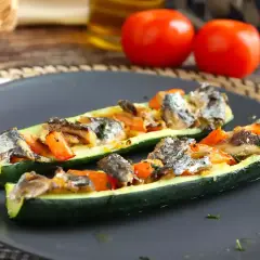 Två halvor av fylld zucchini med fisk och grönsaker på en mörk tallrik.