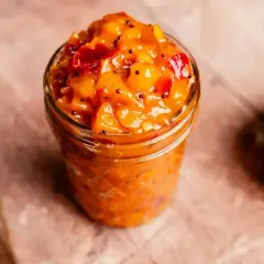 En burk med mango chutney, perfekt för ditt nästa chutney recept. En hel mango och en träsked syns också.