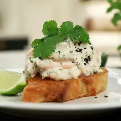 En rostad brödskiva toppad med krämig skagenröra, färska örter, svarta sesamfrön och en limeklyfta. En spännande asiatisk skagen-twist.