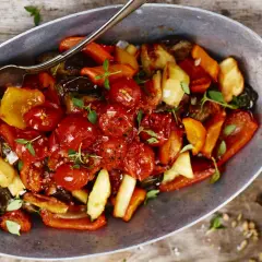 En varm ugnsbakad grönsaksblandning med körsbärstomater, paprika och aubergine, serverad i en metallskål med en sked. En härlig rostad tomatsås gör rätten extra smakrik.