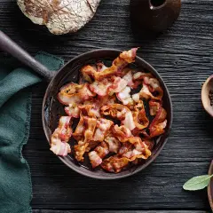 Knaperstekt bacon i panna, redo att avnjutas med nybakat bröd och färska örter.