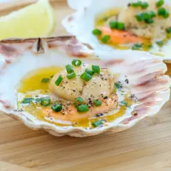 Läckra pilgrimsmusslor i skal, serverade med smält smör, örter och citron. Ett perfekt pilgrimsmusslor recept för en festmåltid.
