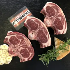 Tre saftiga lammkotletter, vitlök och rosmarin ligger redo för att grilla lammkotletter. En bit focaccia ligger bredvid.
