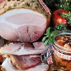 En saftig griljerad skinka i ugn, skuren i skivor, serveras med äppelchutney, en röd äpple och enbärskvist.