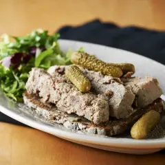 En tallrik med skivad leverpastej på mörkt bröd, toppad med cornichoner och en sallad. Perfekt för ett klassiskt leverpastej recept.