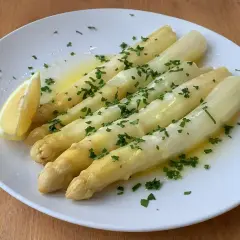 En tallrik med ångad vit sparris, garnerad med hackad persilja och en citronklyfta. En klassisk och delikat rätt.