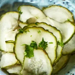 Skivade pressgurkor i en blå skål, toppade med färsk persilja. Ett enkelt och gott pressgurka recept.