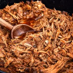 Saftigt pulled pork i en gryta, perfekt för ett gott recept. En träsked ligger i köttet.