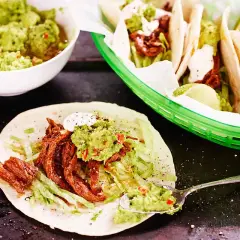 En läcker pulled beef taco med guacamole och strimlad sallad. En skål med mer guacamole och en limeklyfta syns också.