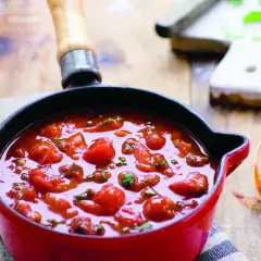 En röd kastrull fylld med en smakrik italiensk tomatsås med hela körsbärstomater och örter. En sked med sås ligger bredvid.