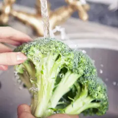 Färska broccolibuketter sköljs under rinnande vatten, redo för ett hälsosamt broccoli recept.