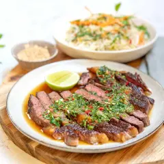 Skivad asiatisk entrecote med örtig sås, lime och en skål med ris.