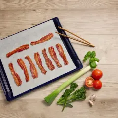 Bacon i ugn på bakplåtspapper, redo att serveras med färska grönsaker.