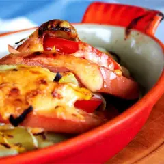 Baked falukorv with melted cheese and tomatoes in a red dish.