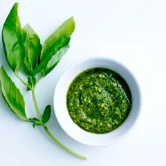 En skål med hemgjord egen pesto bredvid färska basilikablad.