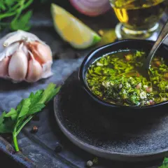 En skål med färsk chimichurri, redo att förhöja din nästa måltid. Ingredienser som vitlök, persilja och citron syns i närheten.