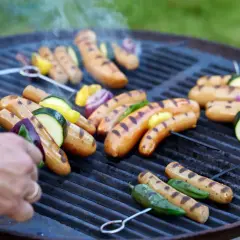Grilla korv med grönsaker på en kolgrill. Röken stiger och ger en härlig doft.