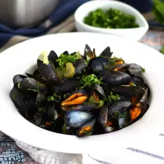 En skål med ångade musslor, moules marinières, garnerade med färsk persilja och serverade med en sidokål.