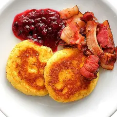 Två gyllene potatisbullar airfryer serveras med rårörda lingon och knaperstekt bacon.