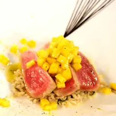 Röda skivor av tonfisk med tärnad mango ovanpå, serverade på ris. En utsökt kombination av tonfisk och mango.
