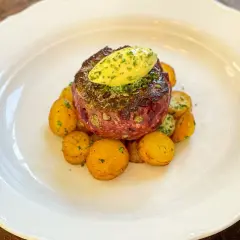 Halstrad råbiff med smör och små, gyllene potatisar på en vit tallrik. En läcker rätt som ser ut att smälta i munnen.