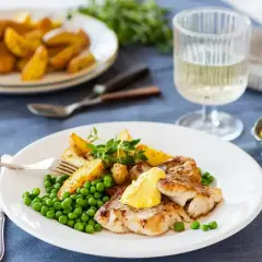 Friterad fisk med klyftpotatis och gröna ärtor, toppad med en klick egen remouladsås. Ett glas vitt vin står bredvid.
