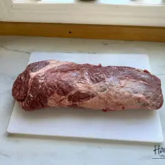 En rå, marmorerad brisket svenska ligger på en vit skärbräda.