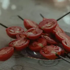 Halverade tomater på spett, redo för grillen. En stapel tallrikar syns till vänster.