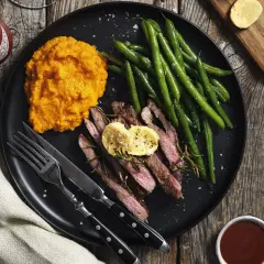 Skivad biff med smör, gröna bönor och sötpotatispuré. En liten flaska Tabasco och en skål med sås antyder ett hemligt, kryddigt tillägg till denna måltid.