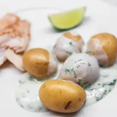 En tallrik med stuvad potatis, fisk och en limeklyfta. Potatisen är krämig och toppad med dill.