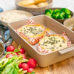 Två runda camembertostar i ugn, toppade med örter, serveras med rädisor, cornichoner och broccoli.