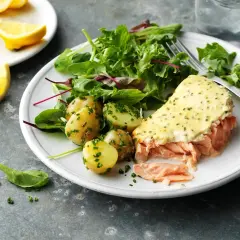 En tallrik med pulled lax, potatis och sallad. En citronskiva ligger bredvid.