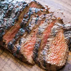 Skivad, grillad flankstek med vackra grillränder och en härlig röd kärna, redo att serveras med chimichurri.