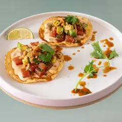 Två läckra tostadas med tonfisk tartar och avocado, toppade med koriander och en krämig sås. En limeklyfta ligger bredvid.