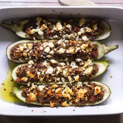 Fyra halverade zucchinis fyllda med en smakrik blandning och toppade med fetaost, redo att avnjutas som gratinerad zucchini.