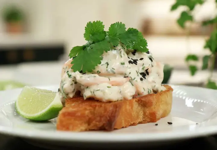 En rostad brödskiva toppad med krämig skagenröra, färska örter, svarta sesamfrön och en limeklyfta. En spännande asiatisk skagen-twist.