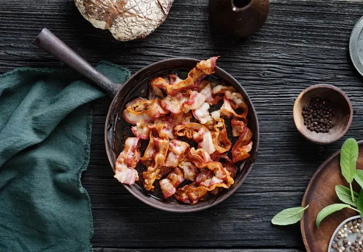 Knaperstekt bacon i panna, redo att avnjutas med nybakat bröd och färska örter.