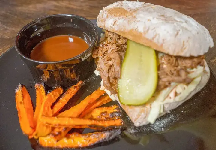 En saftig pulled pork-macka med krispiga sötpotatispommes och en skål med härlig sås till pulled pork.