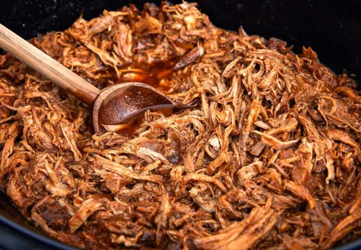 Saftigt pulled pork i en gryta, perfekt för ett gott recept. En träsked ligger i köttet.