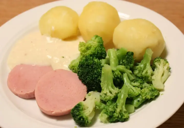 En tallrik med kokt falukorv med pepparrotssås, potatis och broccoli. En klassisk svensk middag.