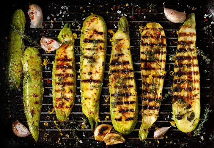 Grillad zucchini med vitlök, örter och citronzest på en grillpanna. Perfekt tillbehör för sommaren.
