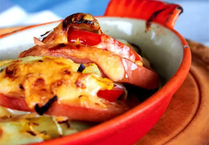 Baked falukorv with melted cheese and tomatoes in a red dish.