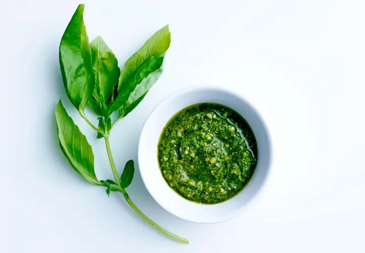 En skål med hemgjord egen pesto bredvid färska basilikablad.