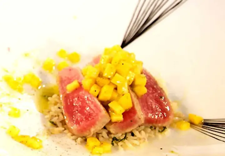 Röda skivor av tonfisk med tärnad mango ovanpå, serverade på ris. En utsökt kombination av tonfisk och mango.