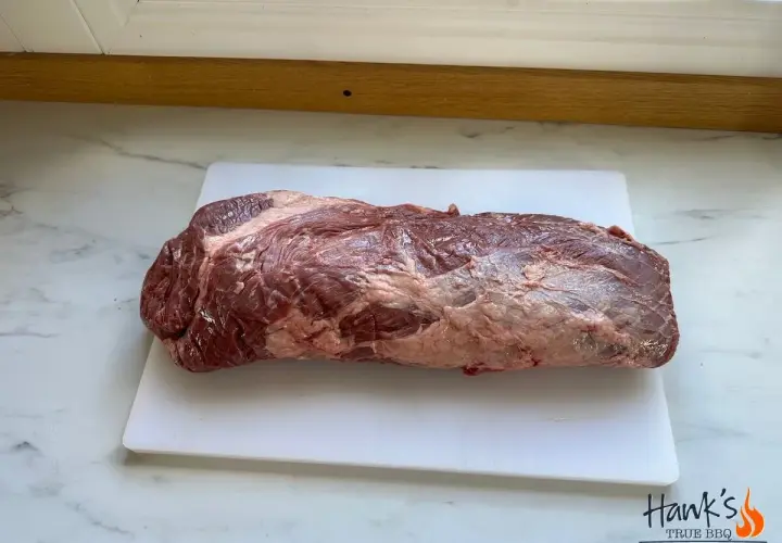En rå, marmorerad brisket svenska ligger på en vit skärbräda.