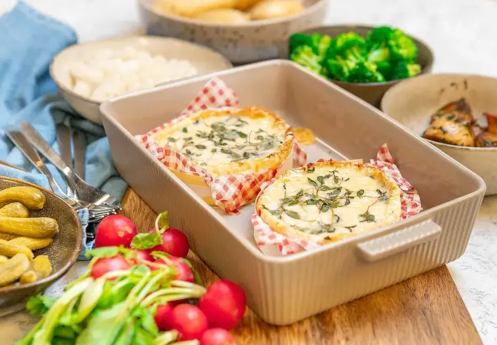 Två runda camembertostar i ugn, toppade med örter, serveras med rädisor, cornichoner och broccoli.