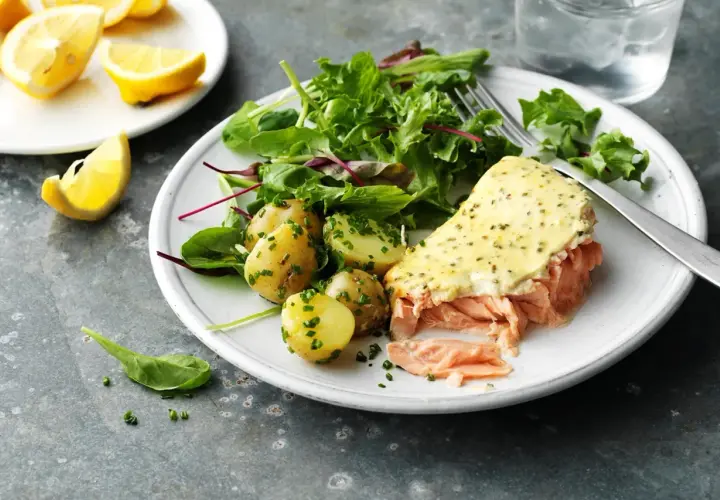 En tallrik med pulled lax, potatis och sallad. En citronskiva ligger bredvid.
